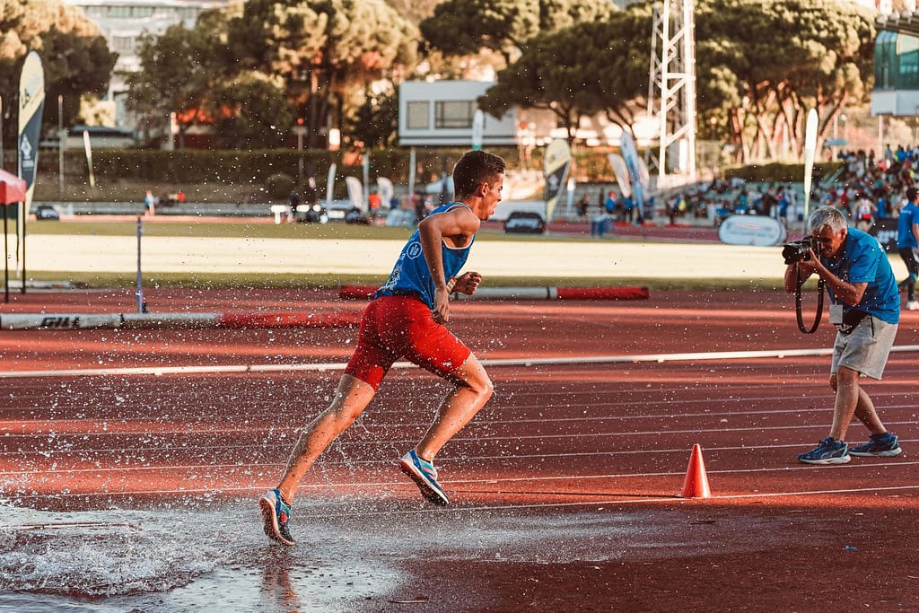 Energetic male athlete sprinting through water on a sunny day track, capturing the essence of competition.